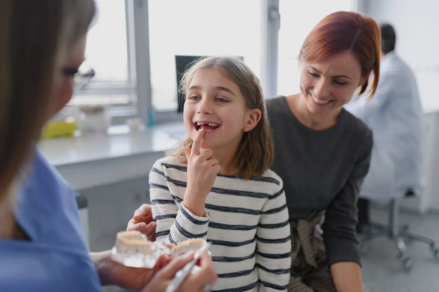 A girl showing her dentist a lost tooth, her mother beside her