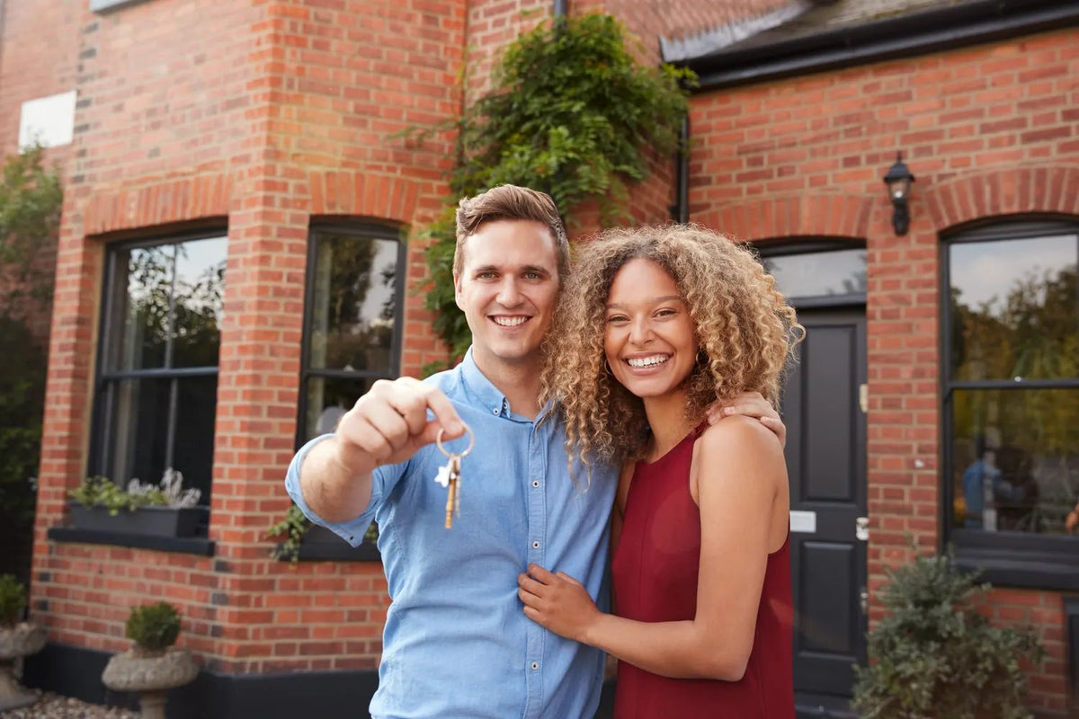 A young couple holding the keys outside their first home