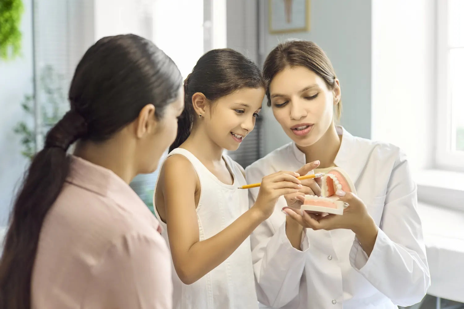 A dentist showing a child and her mother how to brush